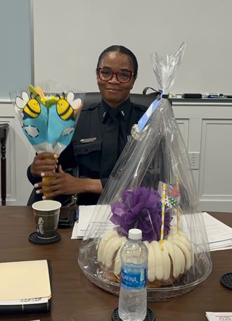 Lieutenant Hold smiles and holds a boquet of flowers while seated behind a bundt cake.