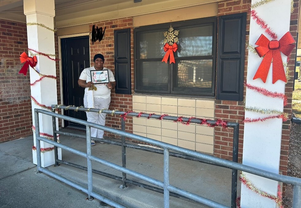 Lady standing on a winning porch holding a certificate for the 2024 door contest.